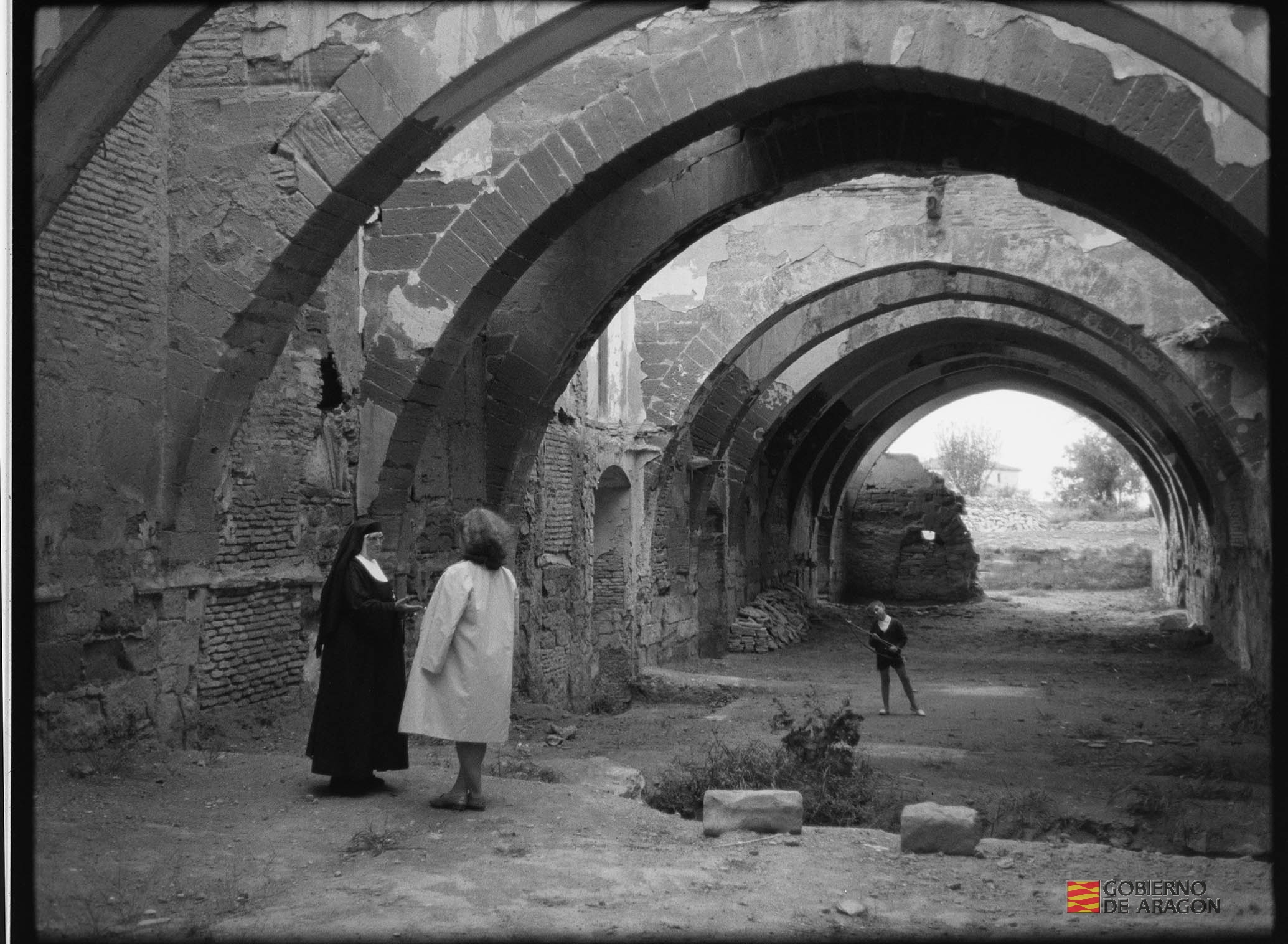 Monasterio de Sigena. Monja, una señora y un niño de espaldas bajo los arcos