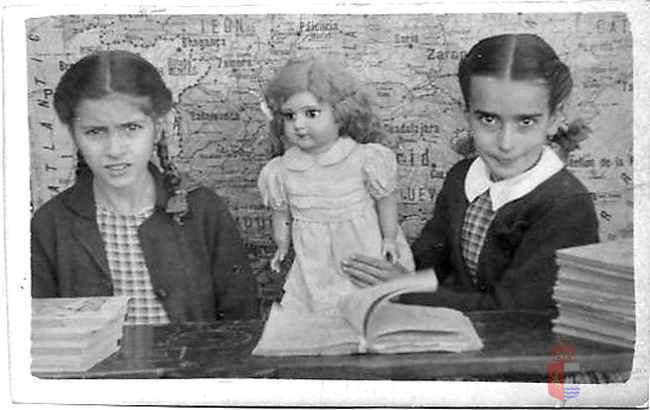 Retrato de dos niñas en la escuela con muñeca y mapa al fondo. La Puebla de Alfindén