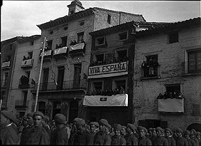 Parada militar en la plaza. Reclutas en formación y balcones engalanados para la ocasión. Mariano Gómez Zamora. Ayerbe