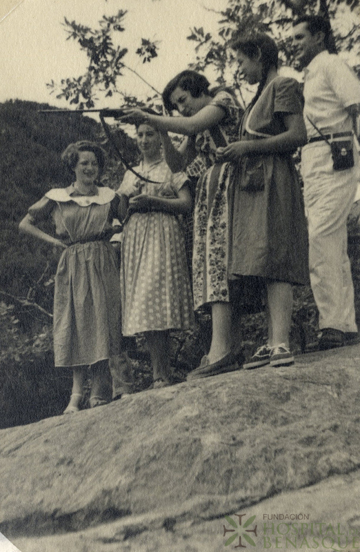 Mujer apuntando con escopeta, acompañada de varias personas