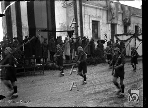 Jóvenes falangistas con casco y fusil, desfilan ante una tribuna de autoridades. Mariano Gómez Zamora