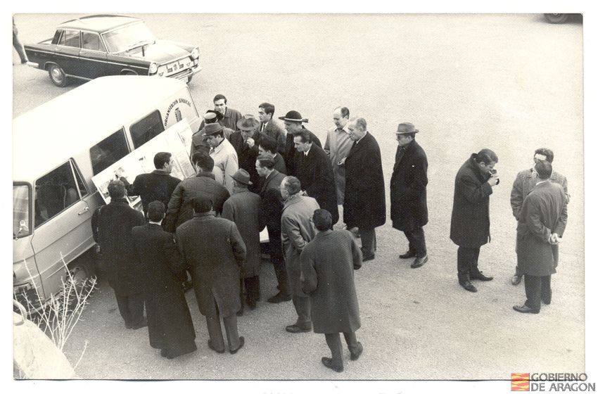 Visita a Teruel del Delegado Nacional de Educación Física y Deportes D. Juan Antonio Samaranch. Embalse del pantano del Arquillo. D. Adolfo Masiá Martínez, delegado provincial de la Organización Sindical, explica sobre un panel ilustrativo algunas actuaciones proyectadas para la práctica de deportes náuticos en el embalse de San Blas. 11 de febrero. San Blas (Teruel)