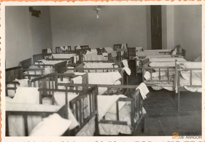 Divulgación y Asistencia. Reparto de cunas para madres necesitadas en la escuela hogar de la Sección Femenina. El acto fue presidido por fray León Villuendas Polo, obispo de la diócesis Teruel-Albarracín, el gobernador civil camarada Aniceto Ruiz Castillejo, y la delegada provincial de la Sección Femenina camarada, Rita Navarro Mínguez. Teruel
