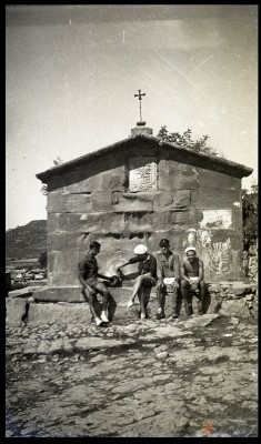 Cuatro hombres sentados. Tras ellos, una fuente con escudo, fecha (1.777) y coronada por una cruz