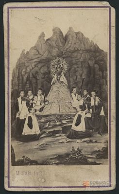 Grupo de niños (monaguillos) con instrumentos rodeando a la Virgen de Montserrat. Al fondo paisaje característico de la Sierra. M.Sala